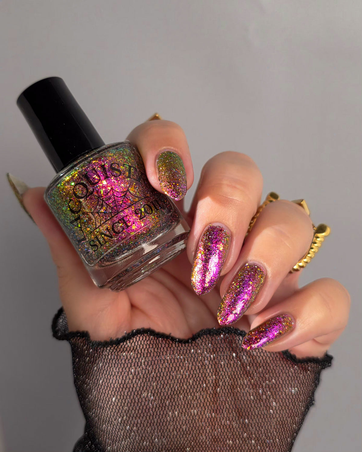 flakie magnetic polish showing red, orange, gold, green flakes, holo glitter, and magnetic effect of fuchsia to purple holding Lacquistry bottle