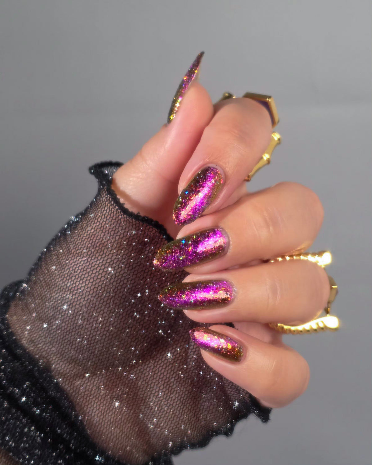 flakie magnetic polish showing red, orange, gold, green flakes, holo glitter, and magnetic effect of fuchsia to purple on hand with black sleeve