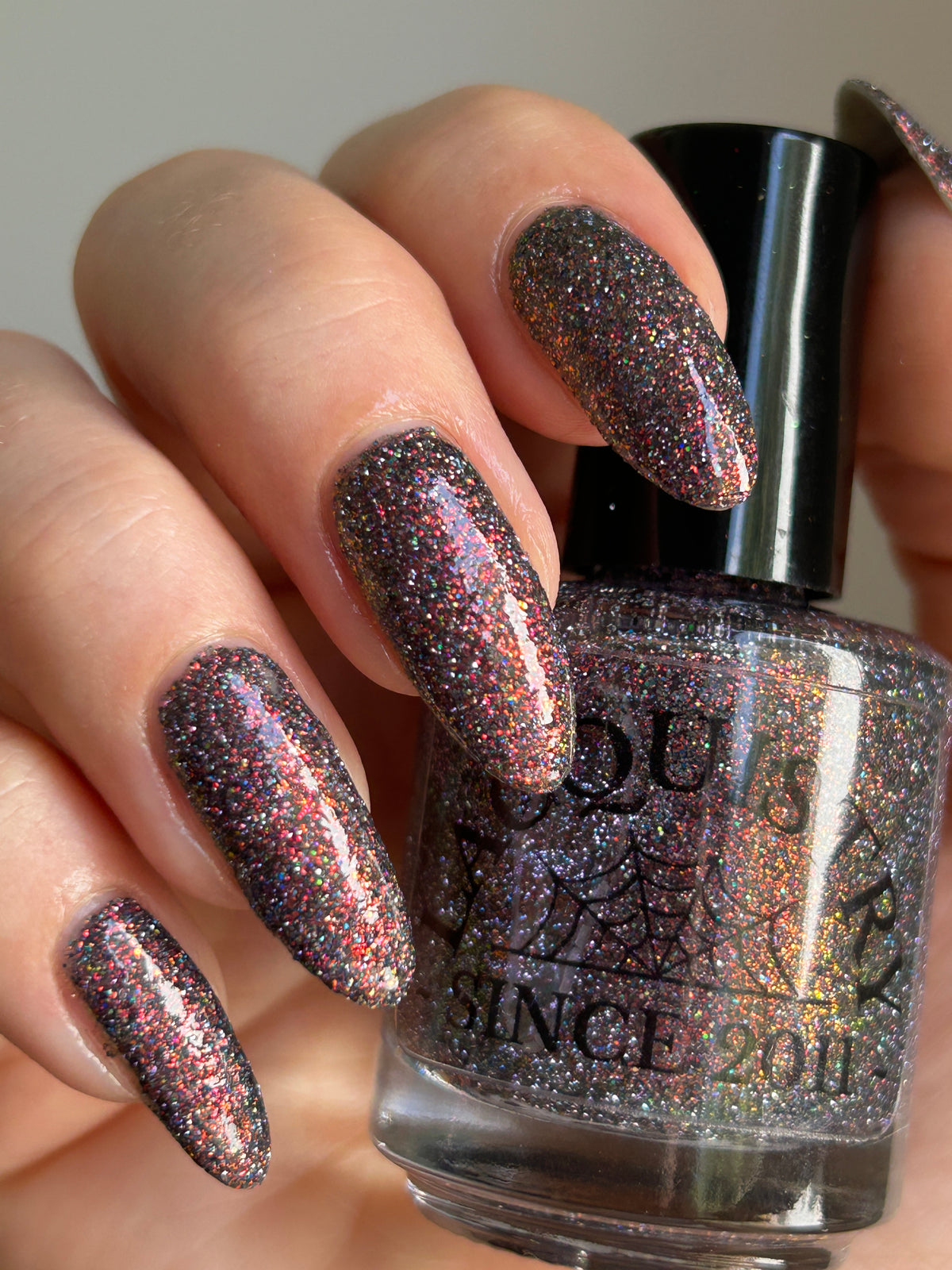 red sparkles with lavender reflective glitter in a dark base over nails holding bottle that says LACQUISTRY SINCE 2011