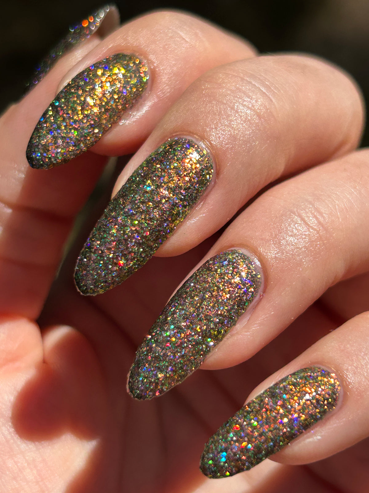 nails painted with sparkly glittery polish showing pink, red, green, gold and orange glitters in a darkened base color with green reflective glitter