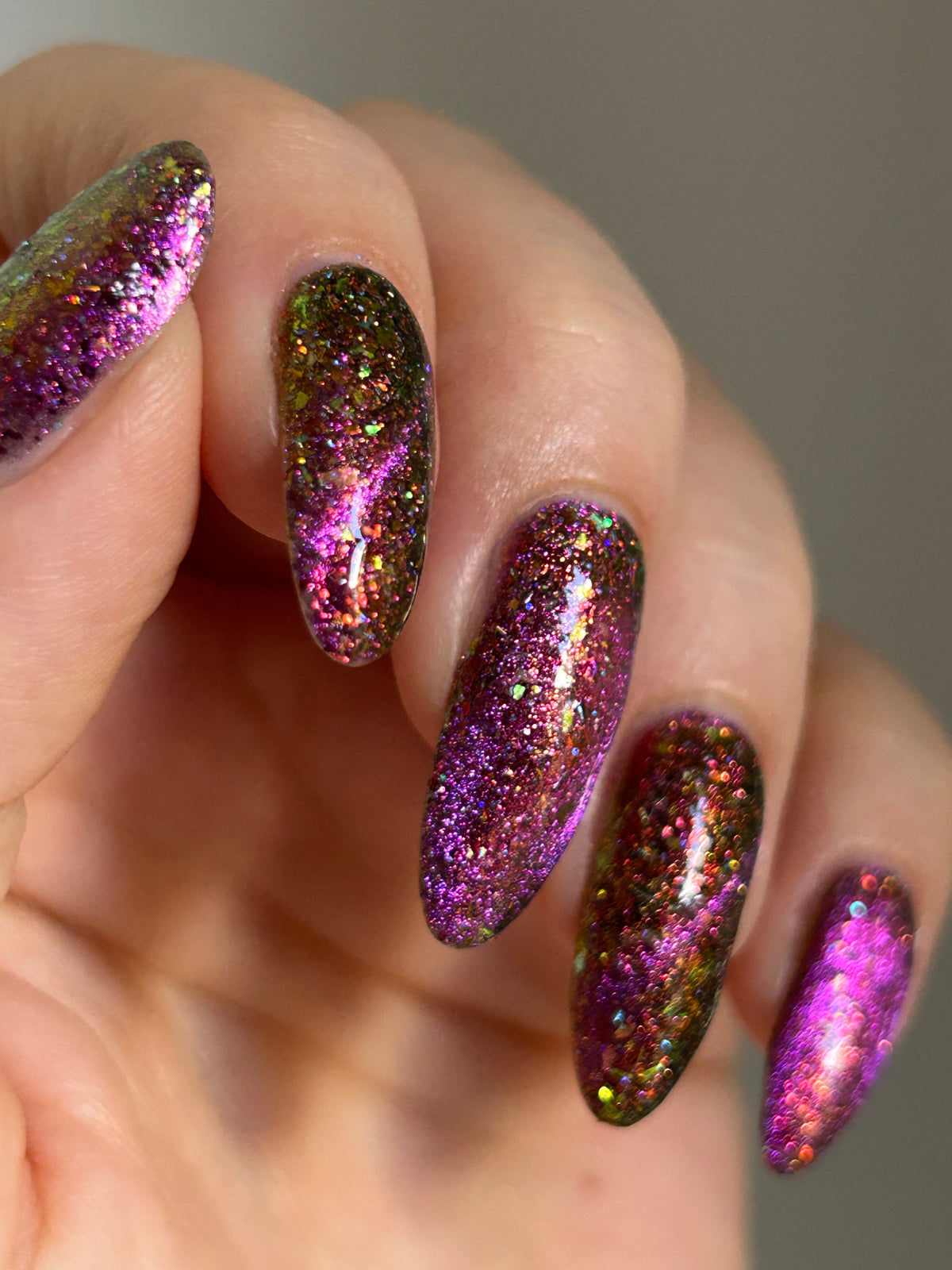 flakie magnetic polish showing red, orange, gold, green flakes, holo glitter, and magnetic effect of fuchsia to purple in varying magnetic styles