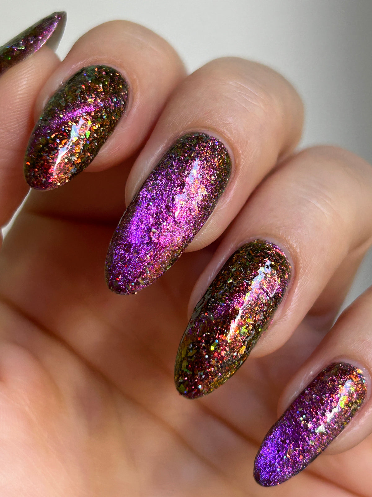 flakie magnetic polish showing red, orange, gold, green flakes, holo glitter, and magnetic effect of fuchsia to purple