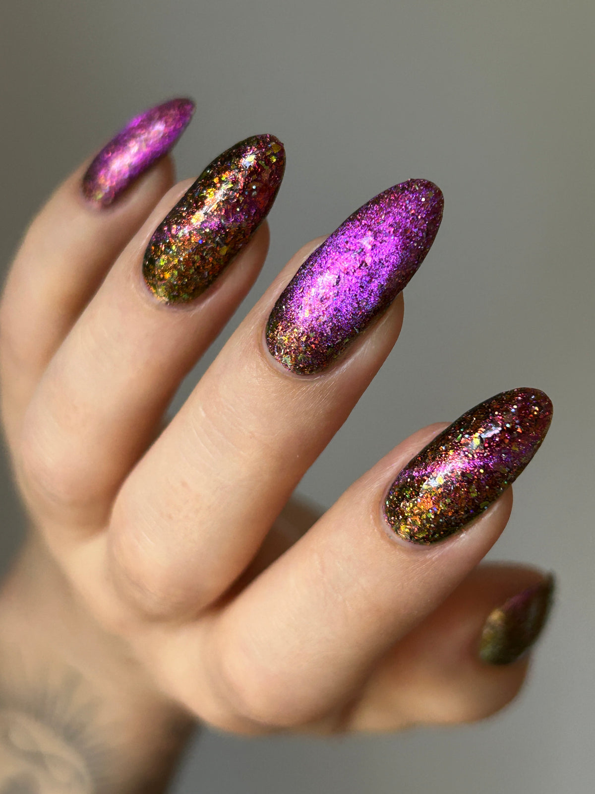 flakie magnetic polish showing red, orange, gold, green flakes, holo glitter, and magnetic effect of fuchsia to purple