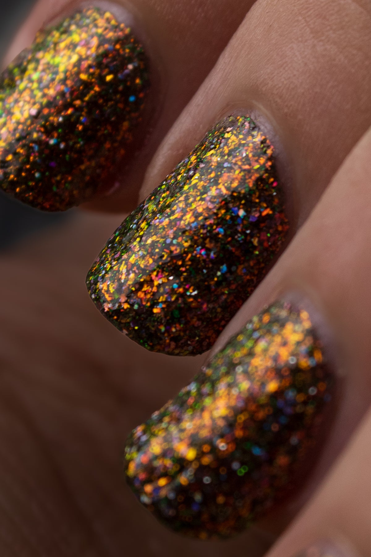 nails painted with sparkly glittery polish showing pink, red, green, gold, lavender holo and orange glitters in a darkened base color with green reflective glitter