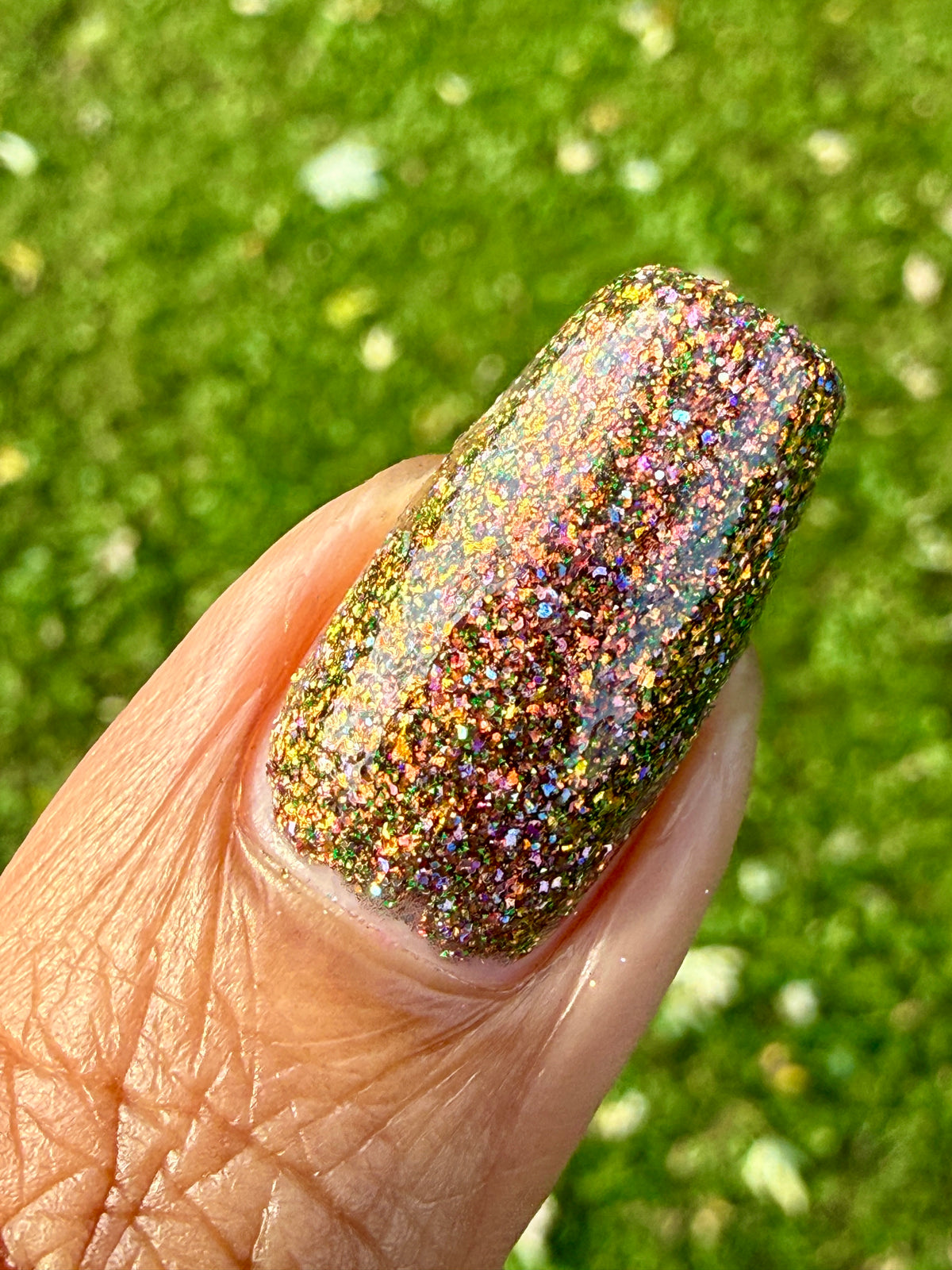 nails painted with sparkly glittery polish showing pink, red, green, gold and orange glitters in a darkened base color with green reflective glitter