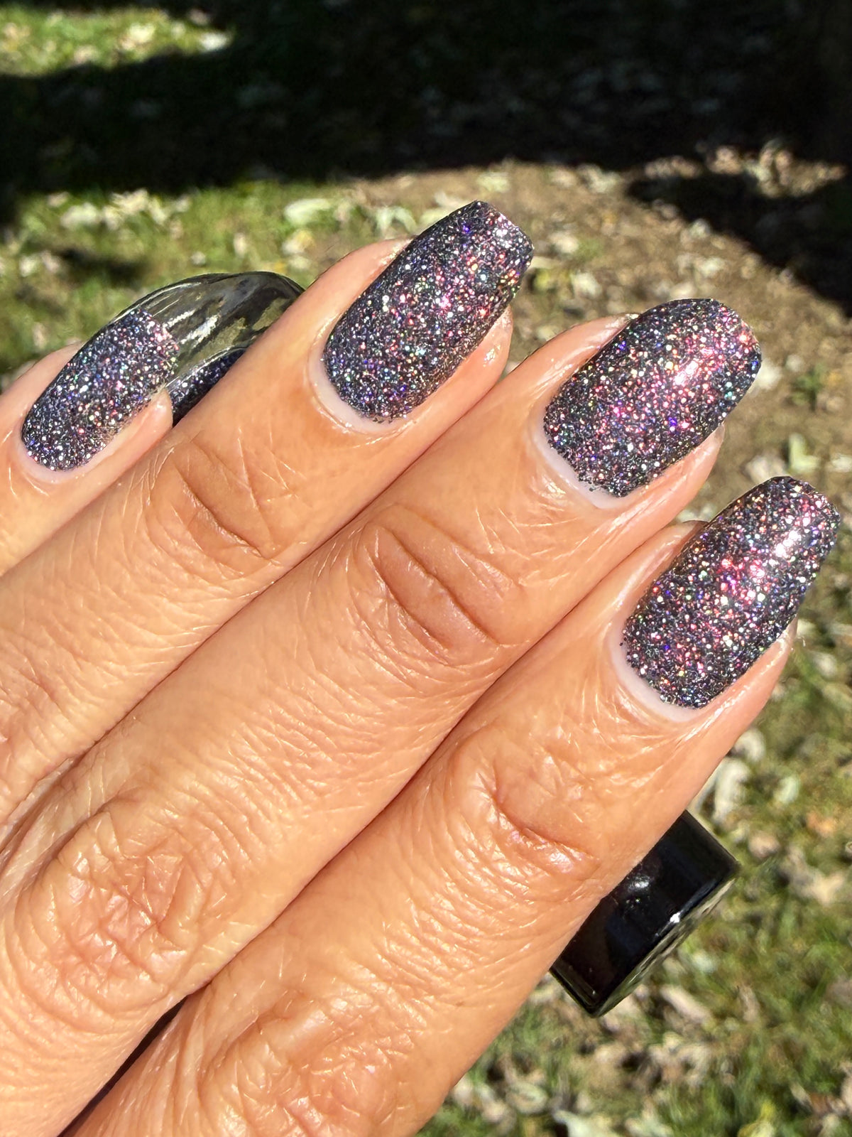red sparkles with lavender reflective glitter in a dark base over nails in sun