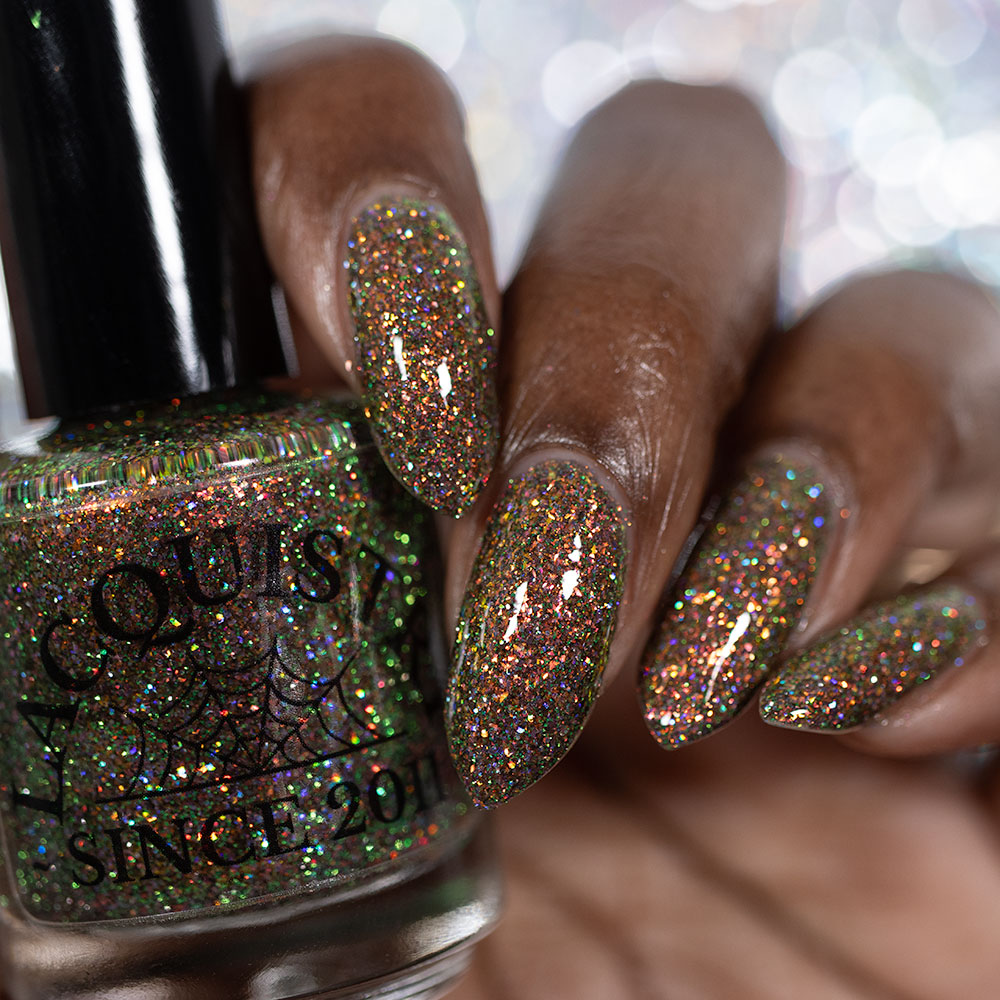 nails painted with sparkly glittery polish showing pink, red, green, gold and orange glitters in a darkened base color with green reflective glitter holding lacquistry bottle