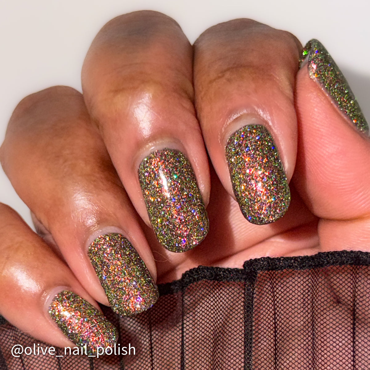 nails painted with sparkly glittery polish showing pink, red, green, gold and orange glitters in a darkened base color with green reflective glitter