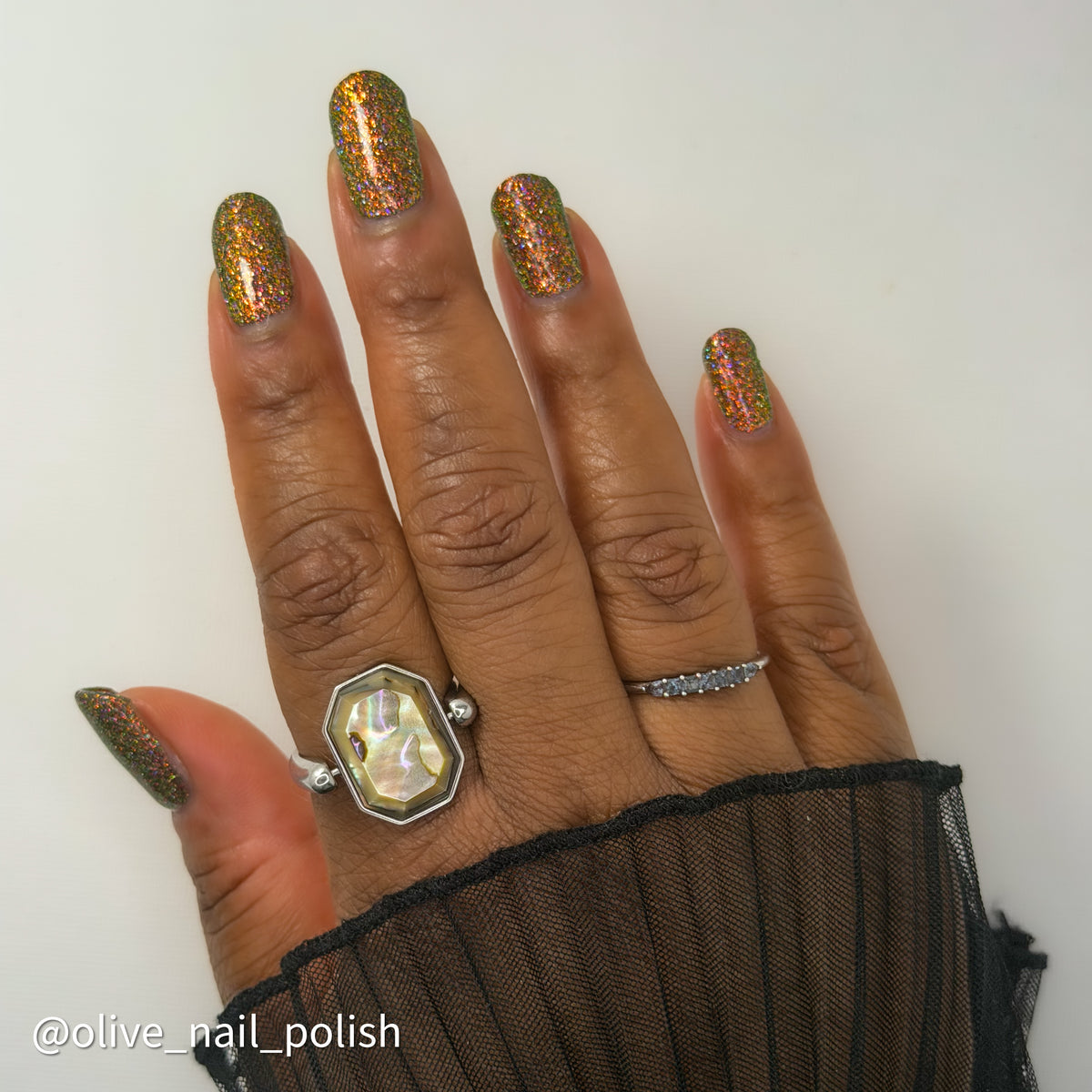 nails painted with sparkly glittery polish showing pink, red, green, gold and orange glitters in a darkened base color with green reflective glitter