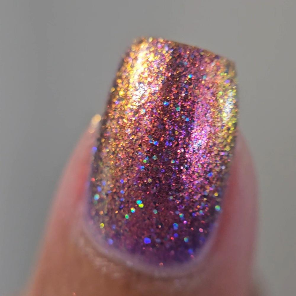 close up picture of medium skin toned fingernail with medium/long square nails wearing metallic purple, pink sparkle nail polish with holo glitter