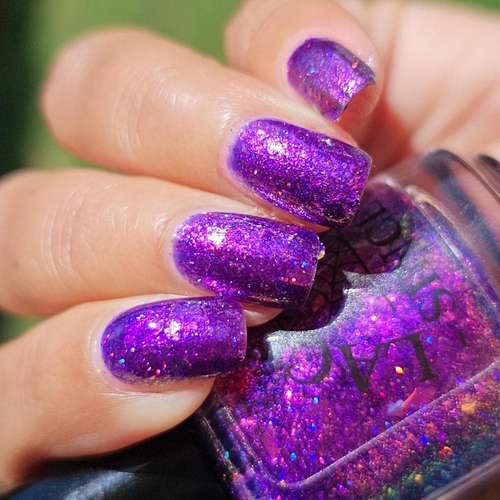closeup of nails painted vibrant purple and violet sparkly nail polish holding a bottle of the same shade, medium skin tone in the sun