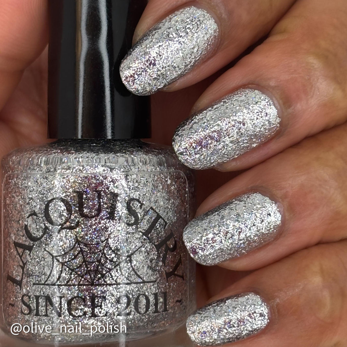 A close-up of a hand with nails painted in a shiny silver glitter nail polish, next to the Lacquistry bottle showing the same sparkling silver formula.