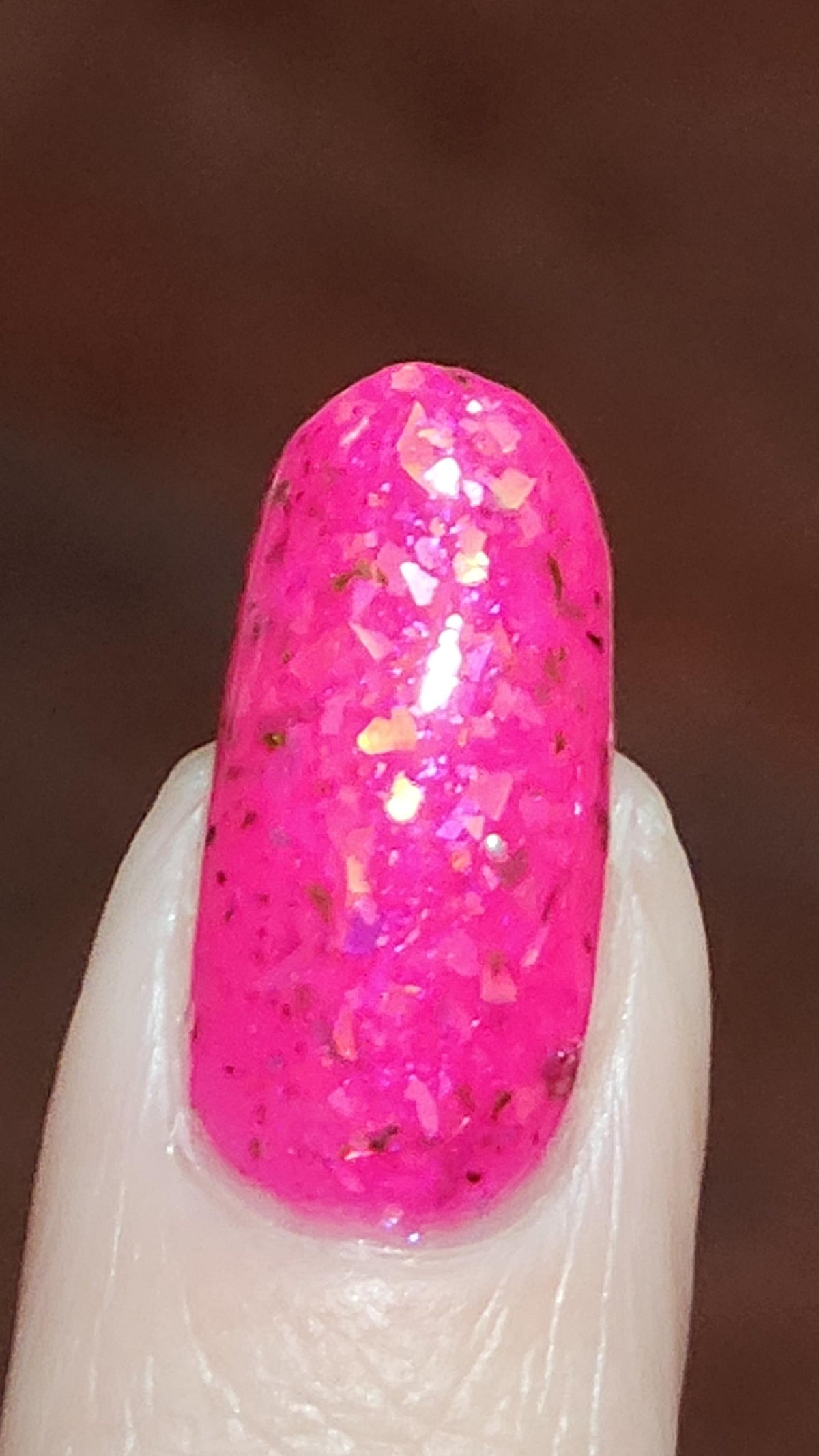 closeup of nail with light skin long nail wearing neon pink flake jelly polish