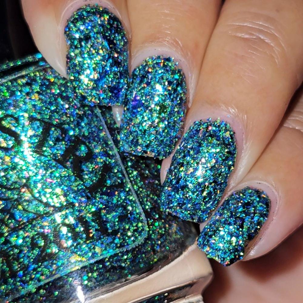 Close-up of a hand with manicured nails painted in a dense, chunky holographic glitter nail polish, with the matching glitter polish bottle shown in the foreground.