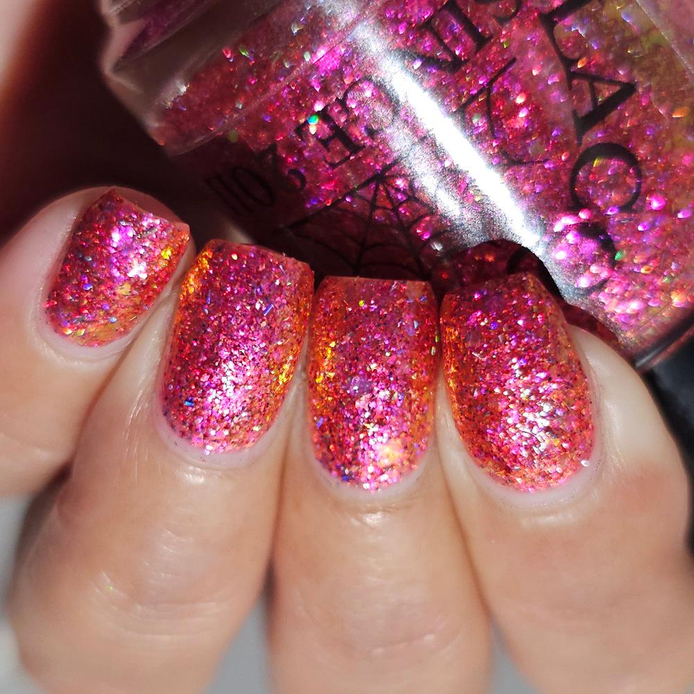medium length square nails on medium skin tone wearing bright pink sparkling flake and glitter nail polish holding a bottle with a spiderweb of the same polish