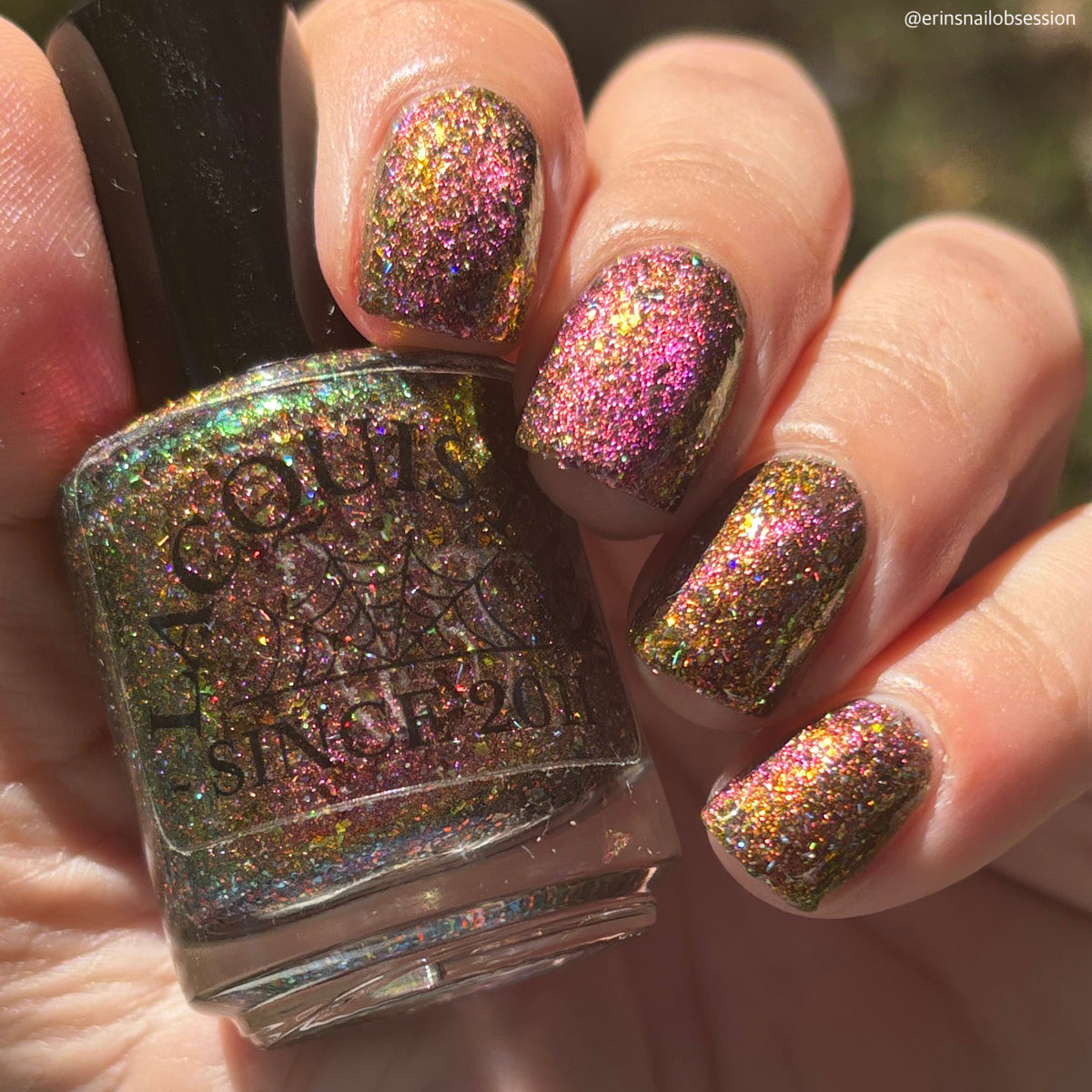 flakie magnetic polish showing red, orange, gold, green flakes, holo glitter, and magnetic effect of fuchsia to purple in the sun holding Lacquistry bottle