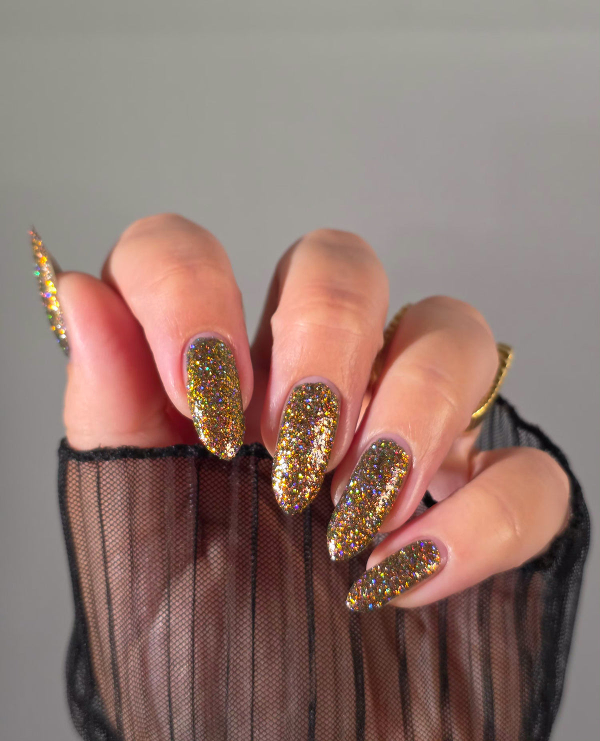nails painted with sparkly glittery polish showing pink, red, green, gold and orange glitters in a darkened base color with green reflective glitter
