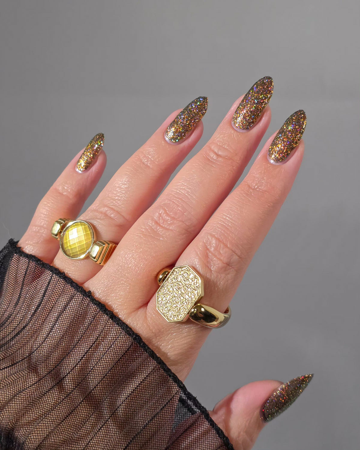 nails painted with sparkly glittery polish showing pink, red, green, gold and orange glitters in a darkened base color