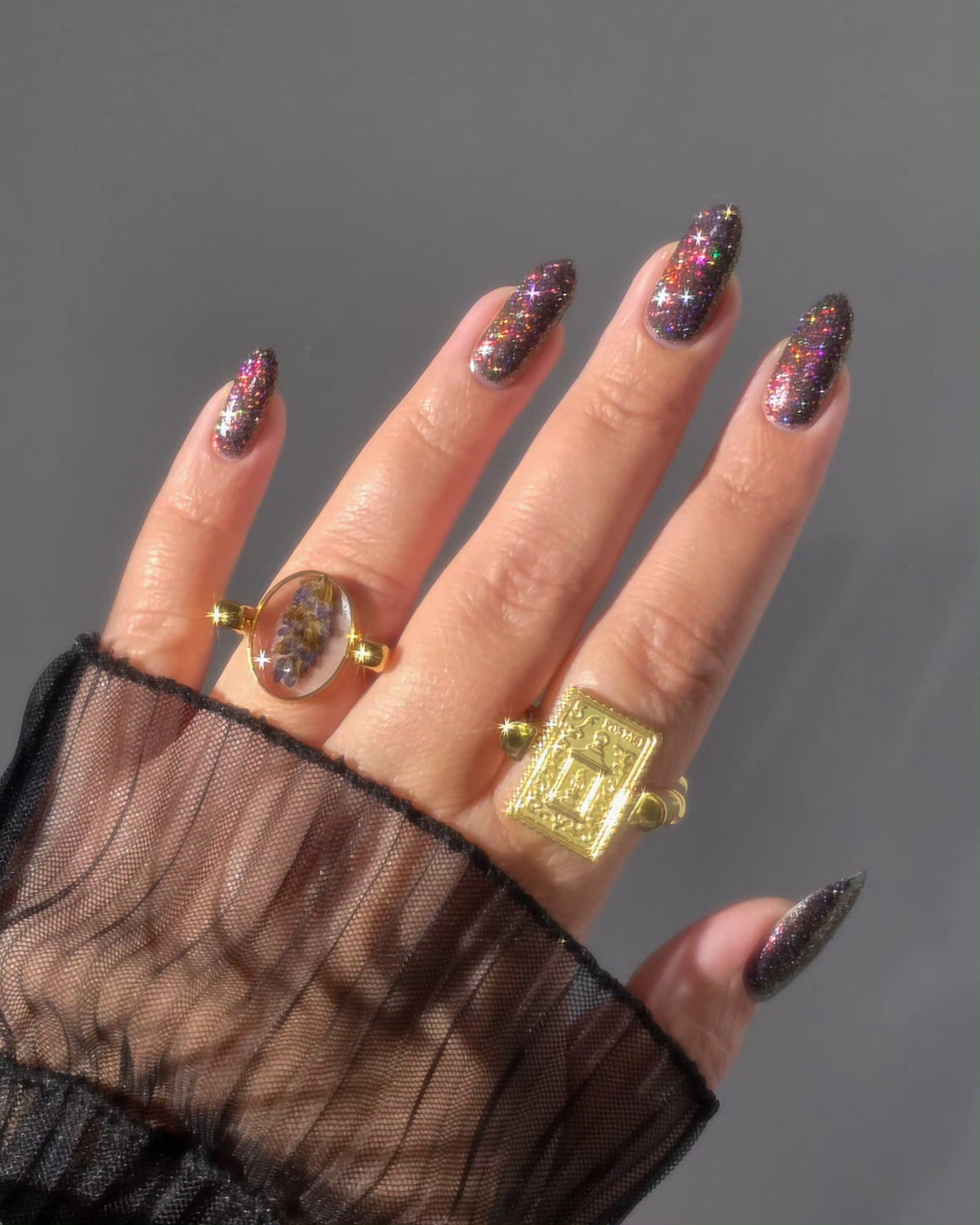 red sparkles with lavender reflective glitter in a dark base over nails wearing rings holding bottle that says LACQUISTRY SINCE 2011