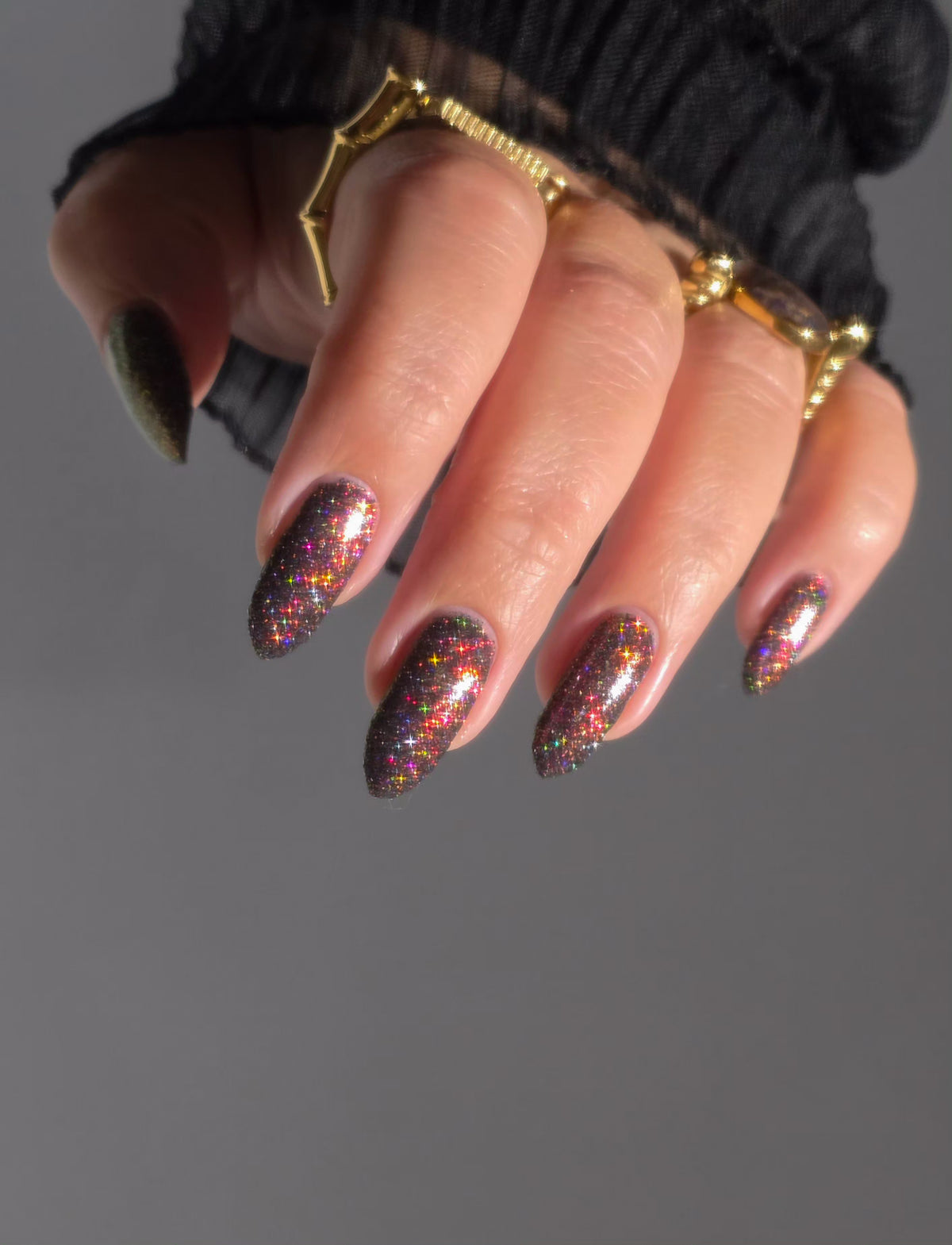 red sparkles with lavender reflective glitter in a dark base over nails with gold rings on fingers