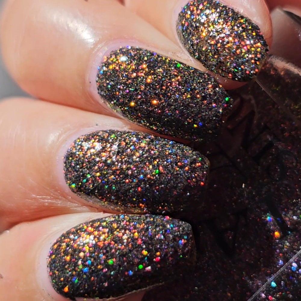 red sparkles with lavender reflective glitter in a dark base over nails holding bottle 