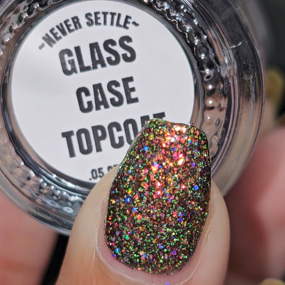 macro of shiny glittery nails holding clear topcoat bottle. bottom label says Glass Case Topcoat