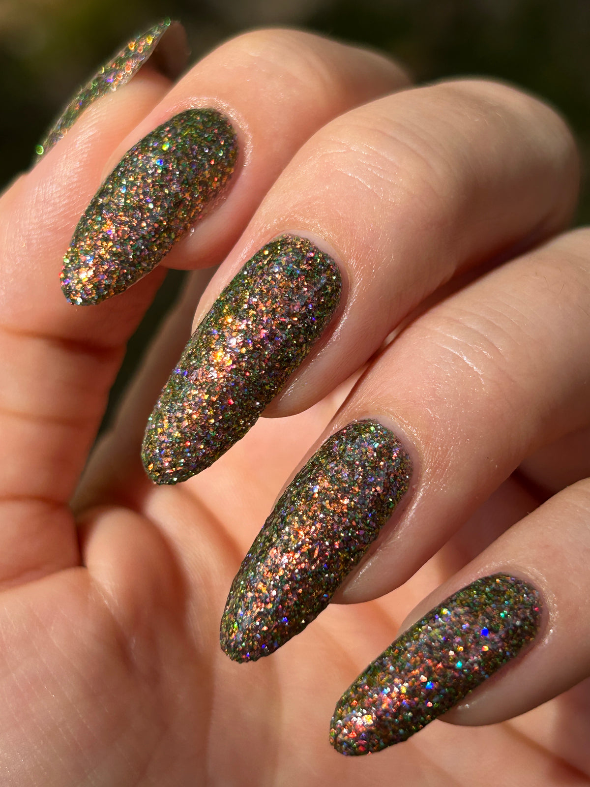 nails painted with sparkly glittery polish showing pink, red, green, gold and orange glitters in a darkened base color with green reflective glitter