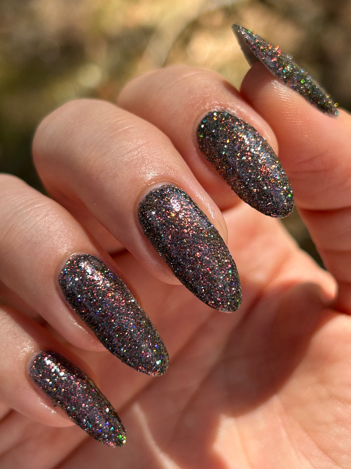 red sparkles with lavender reflective glitter in a dark base over nails in sun
