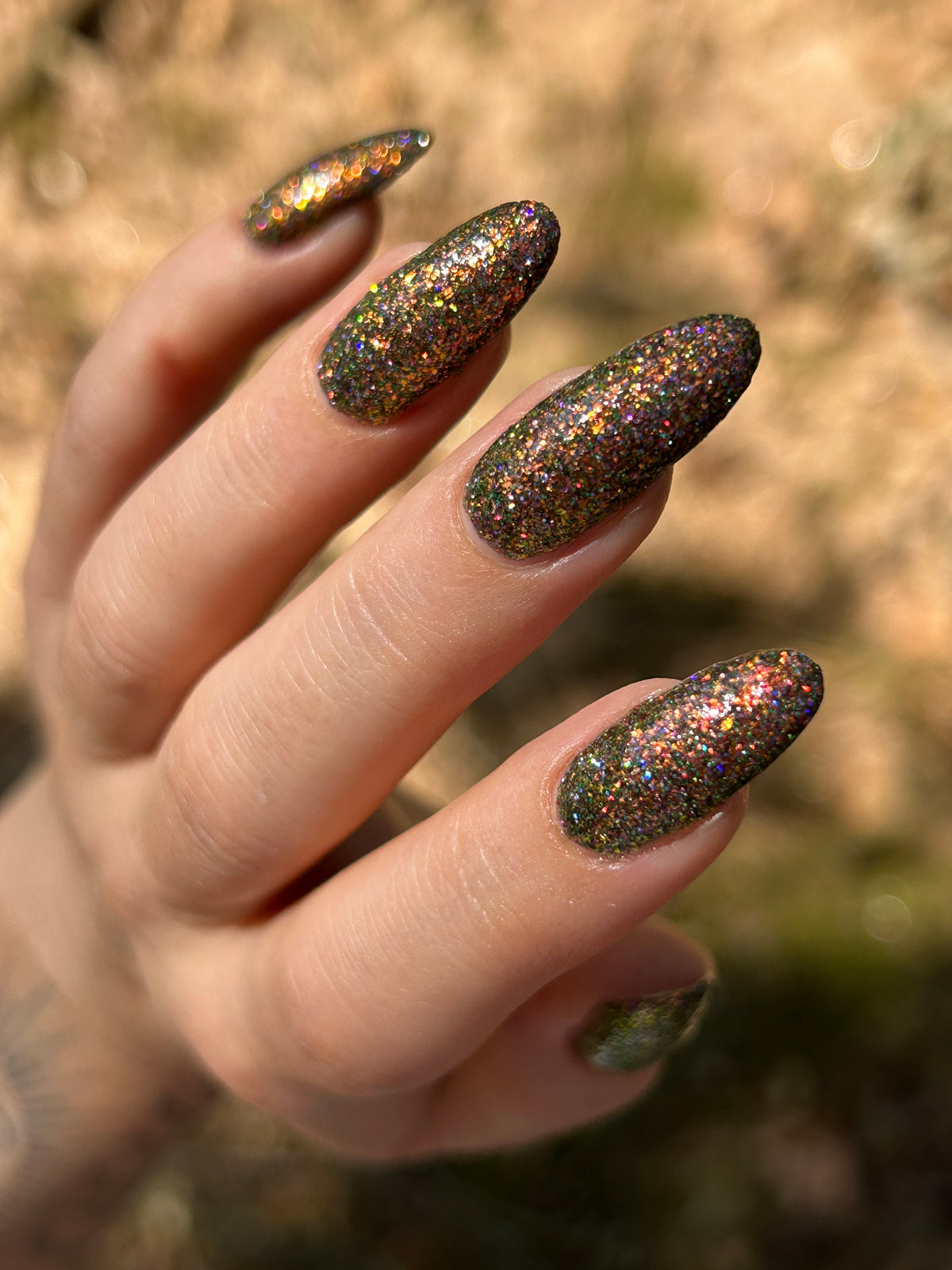 nails painted with sparkly glittery polish showing pink, red, green, gold and orange glitters in a darkened base color with green reflective glitter
