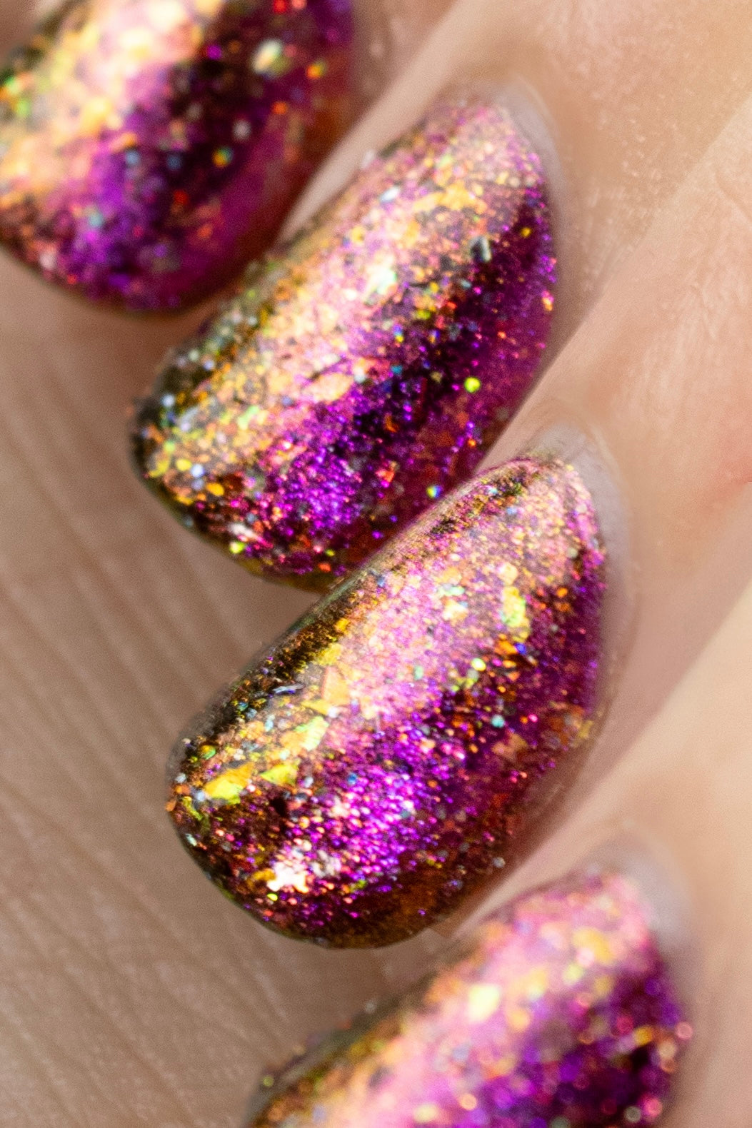 flakie magnetic polish showing red, orange, gold, green flakes, holo glitter, and magnetic effect of fuchsia to purple