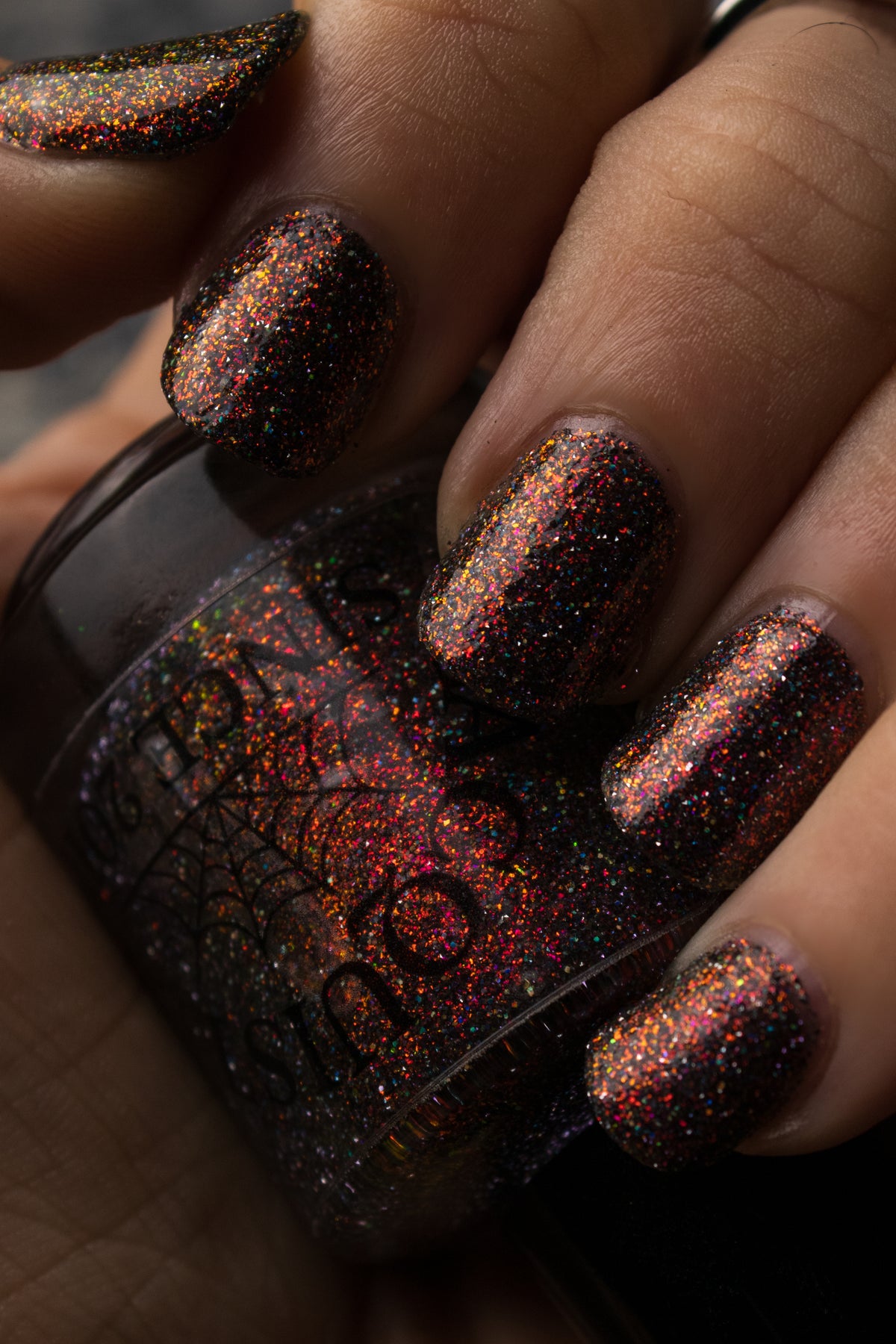 red sparkles in a dark base over nails holding bottle