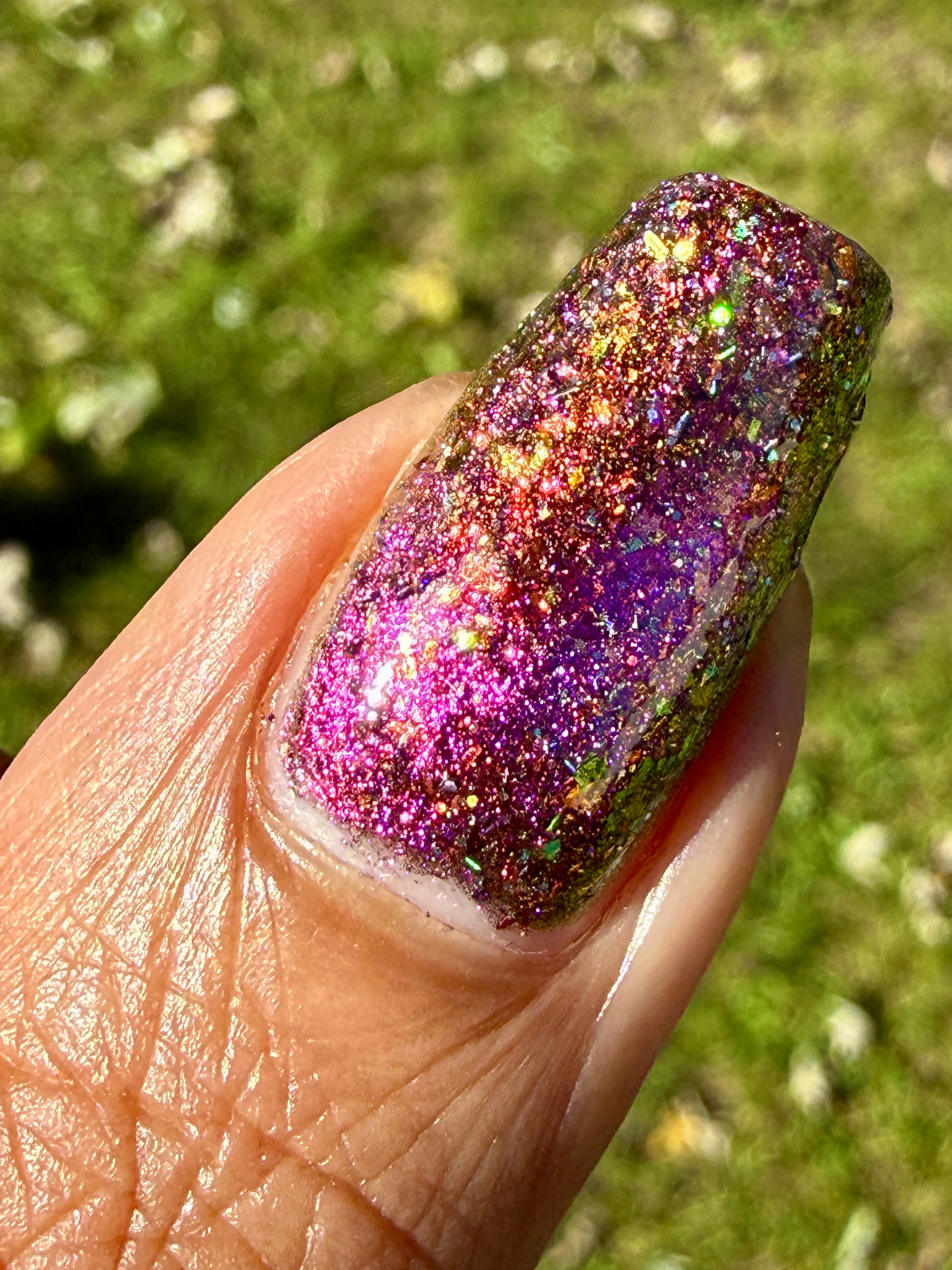 flakie magnetic polish showing red, orange, gold, green flakes, holo glitter, and magnetic effect of fuchsia to purple