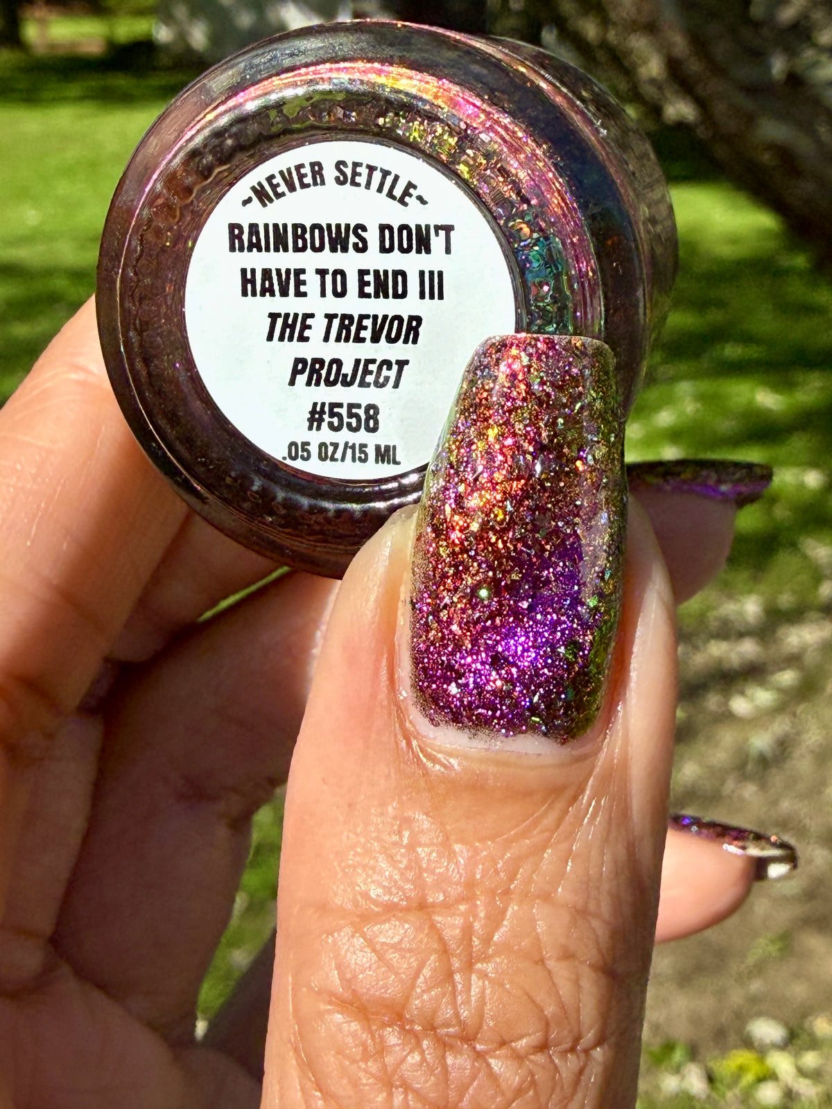 flakie magnetic polish showing red, orange, gold, green flakes, holo glitter, and magnetic effect of fuchsia to purple holding bottle that says rainbows don't have to end III the Trevor Project