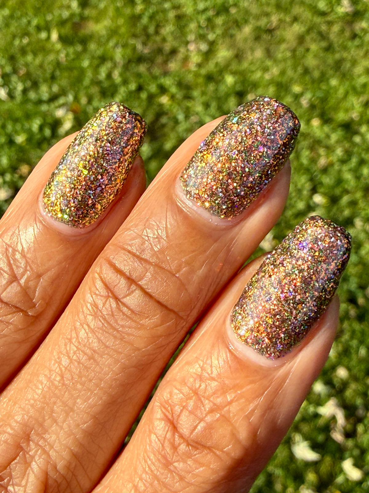 nails painted with sparkly glittery polish showing pink, red, green, gold and orange glitters in a darkened base color with green reflective glitter