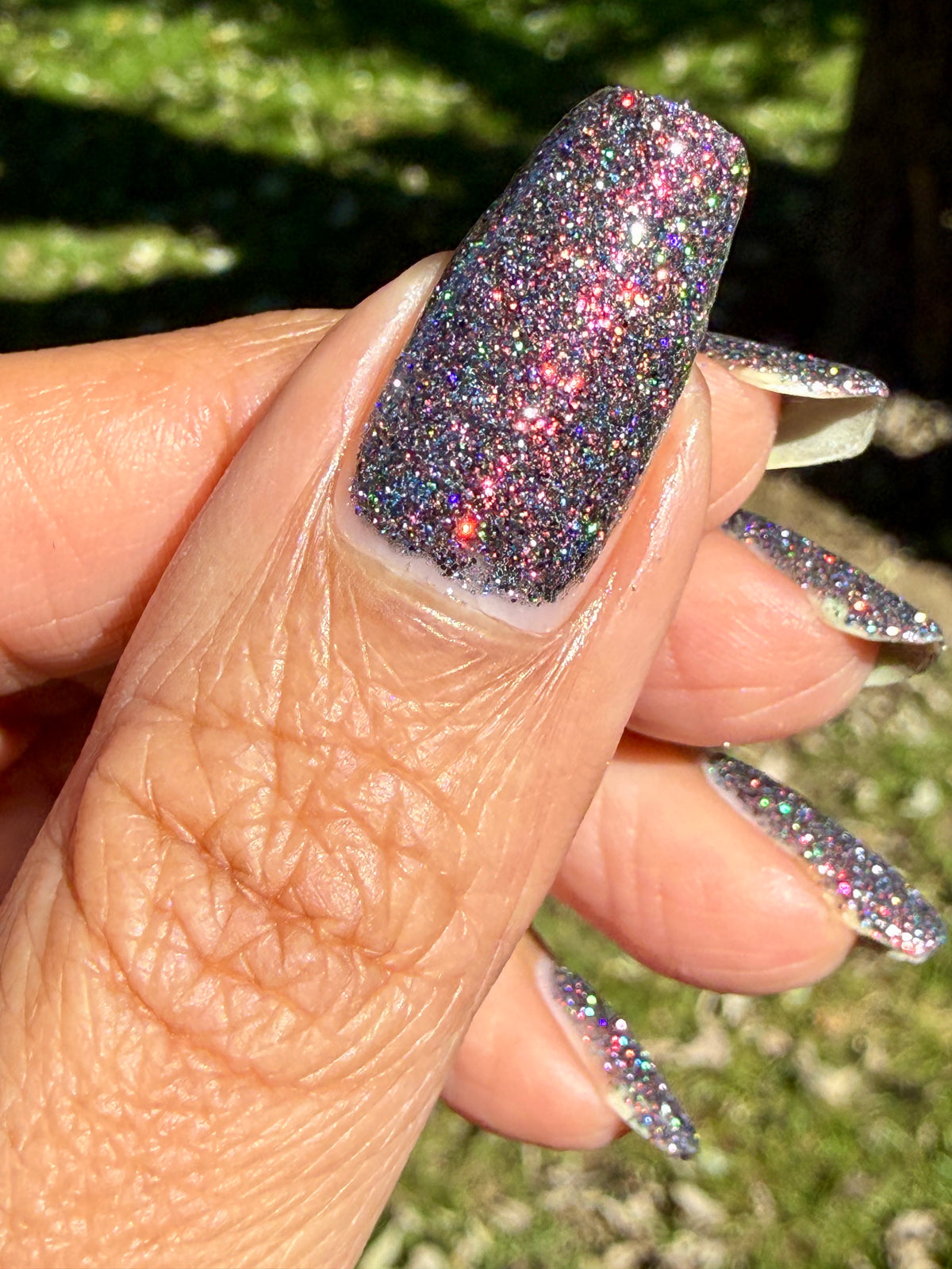 red sparkles with lavender reflective glitter in a dark base over nails outside