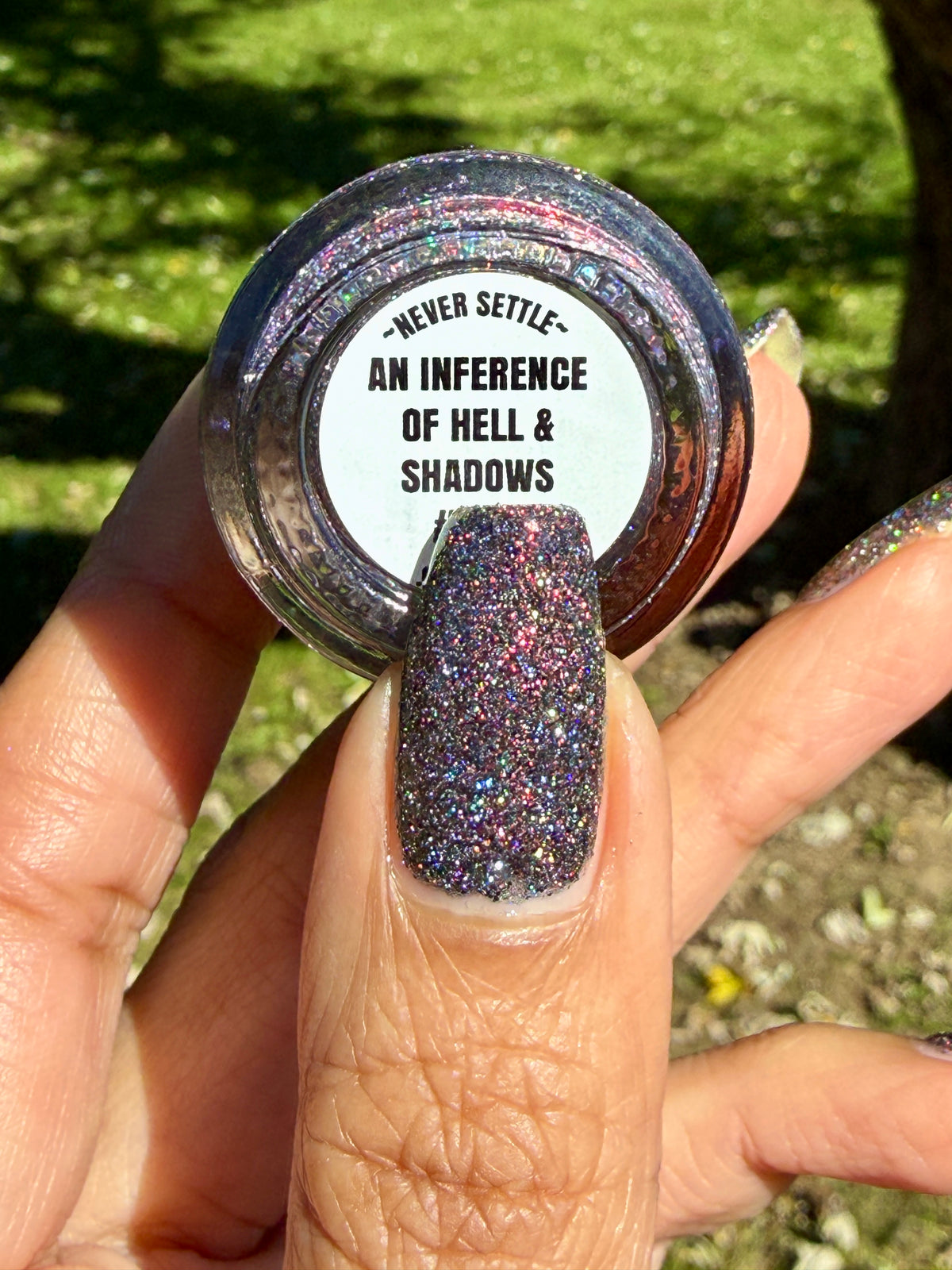 red sparkles with lavender reflective glitter in a dark base over nails holding bottle that says an inference of hell and shadows