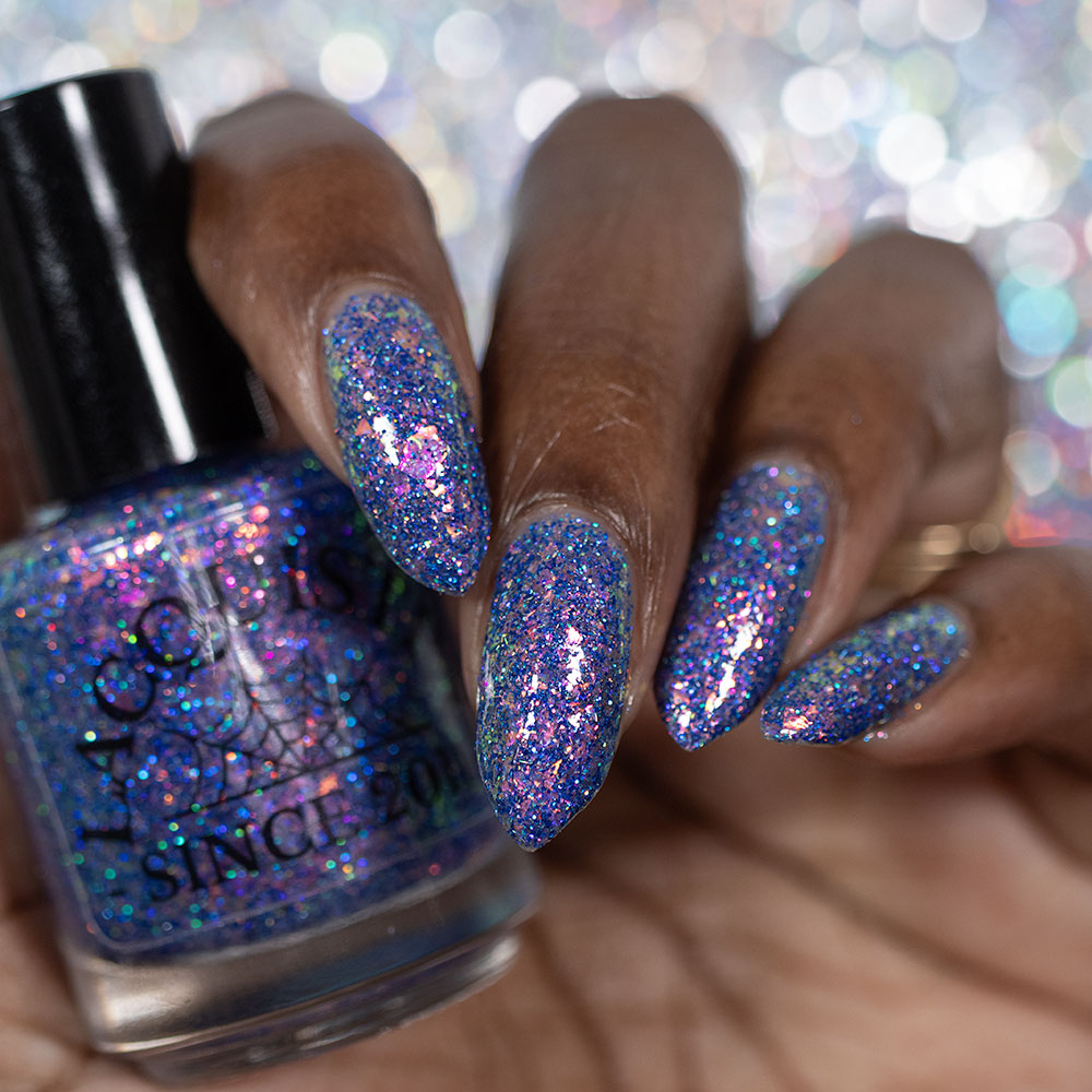 A close-up of a hand with long almond-shaped nails painted in a sparkling holographic purple nail polish, holding a matching glittery nail polish bottle labeled 'SINCE 2011'.