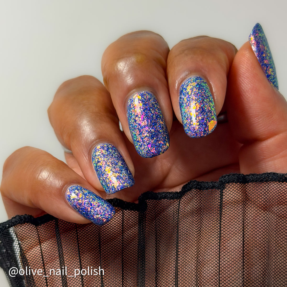 Close-up of a hand with manicured nails painted in a holographic blue glitter nail polish, with a watermark reading @olive_nail_polish in the lower left corner.