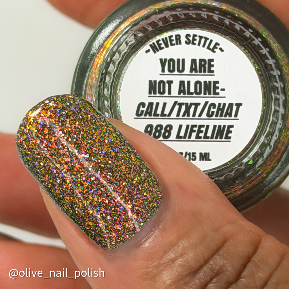 nails painted with sparkly glittery polish showing pink, red, green, gold and orange glitters in a darkened base color with green reflective glitter. bottle says you are not alone