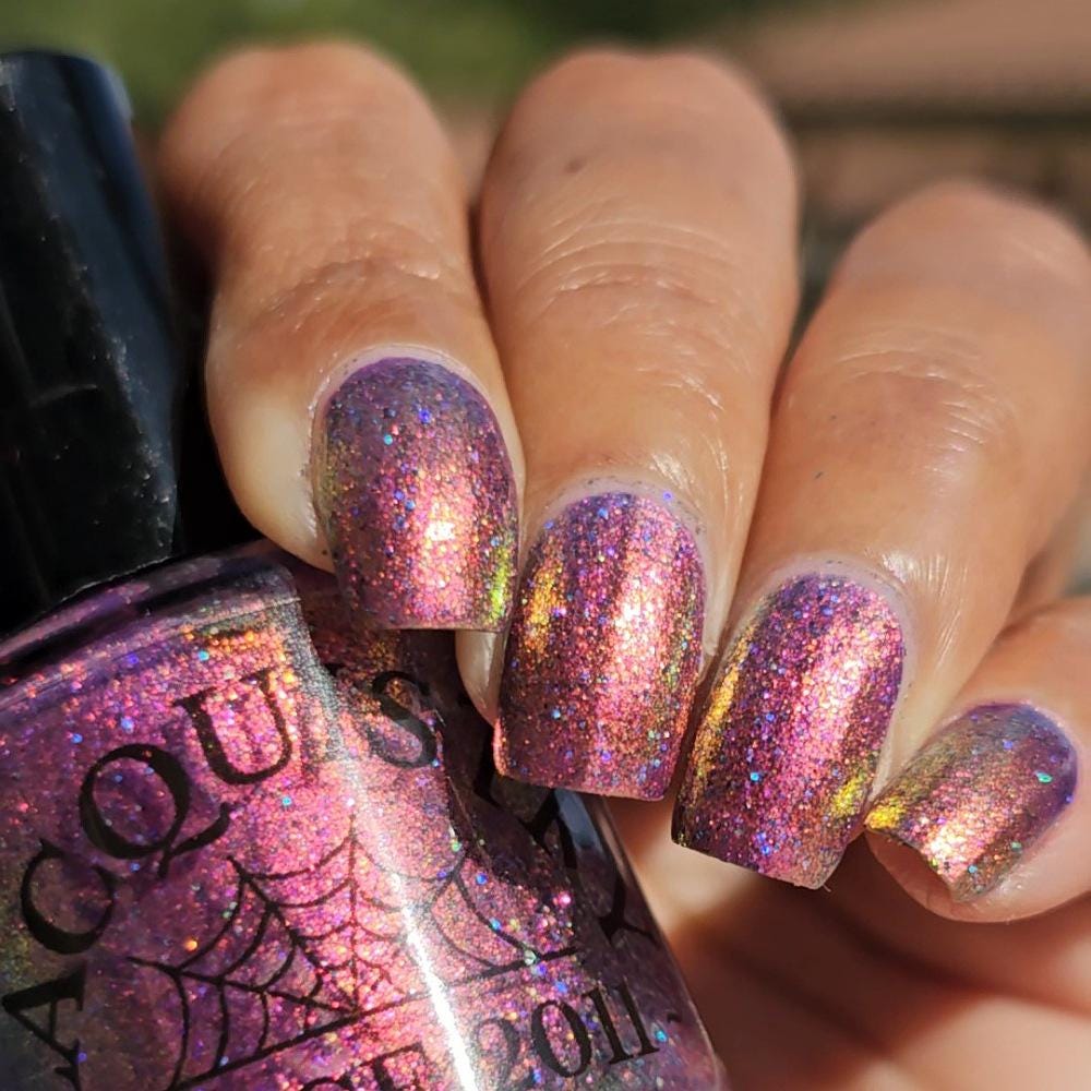 medium skin toned hand with medium/long square nails wearing metallic purple pink sparkle nail polish holding matching bottle of light purple nail polish