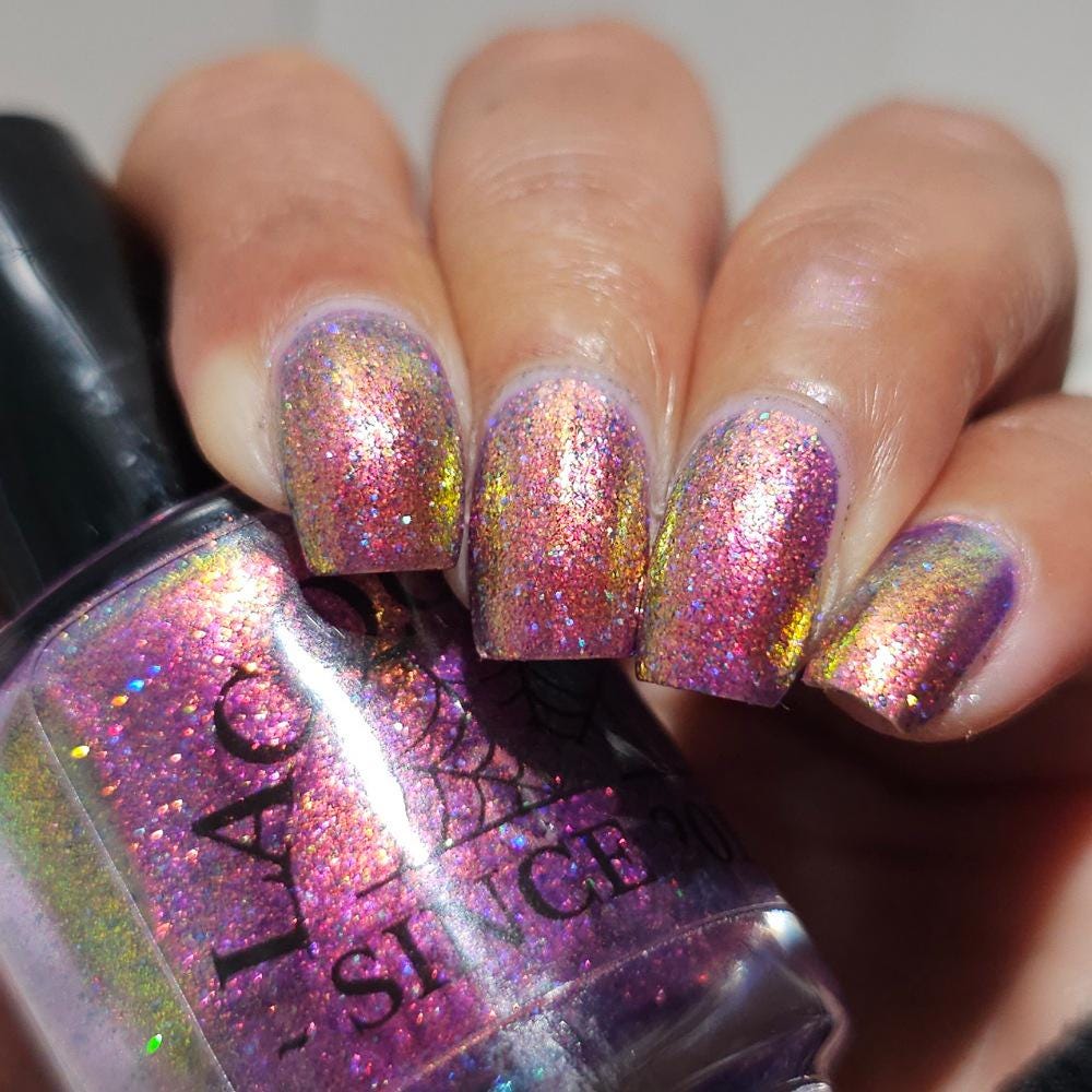 medium skin toned hand with medium/long square nails wearing metallic purple pink sparkle nail polish holding matching bottle of light purple nail polish