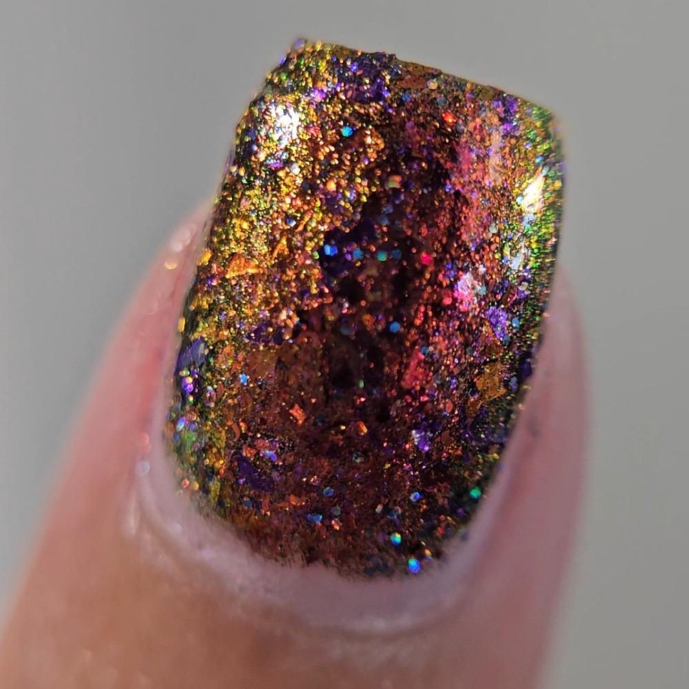 Close-up of a nail with manicured nails painted in a holographic glitter nail polish showing pink, purple, orange, and green iridescent reflections.