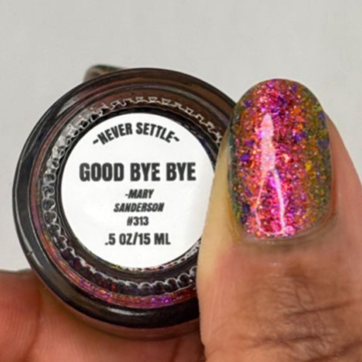 A close-up of a nail polish bottle and a fingernail swatch. The bottle label reads “Never Settle” and “Good Bye Bye - Mary Sanderson #313 .
