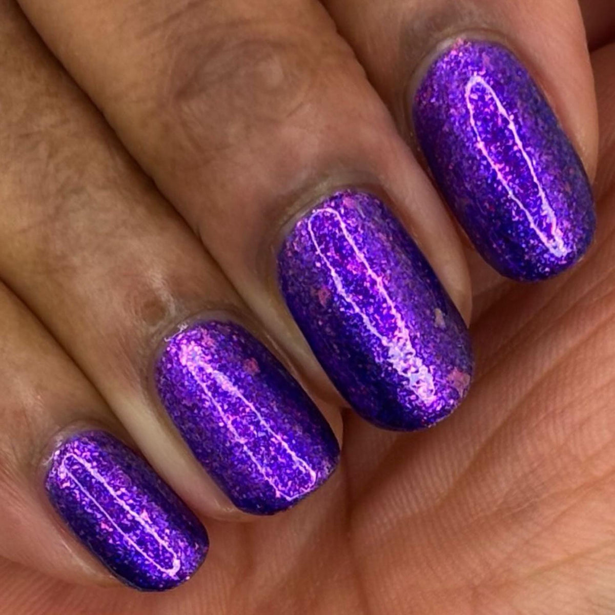 closeup of short nails painted vibrant purple and violet sparkly nail polish dark skin tone 