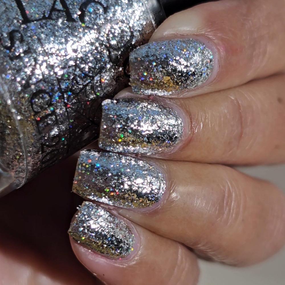A close-up of a hand with nails painted in a sparkling silver glitter nail polish, with the matching glitter bottle partially visible on the left.