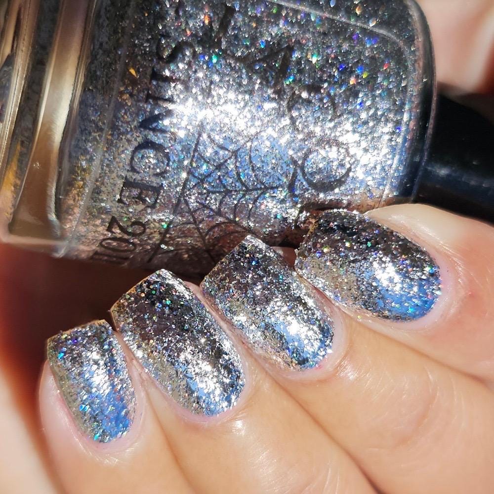 A close-up of a hand with nails painted in a silver glitter nail polish, next to the bottle of nail polish.