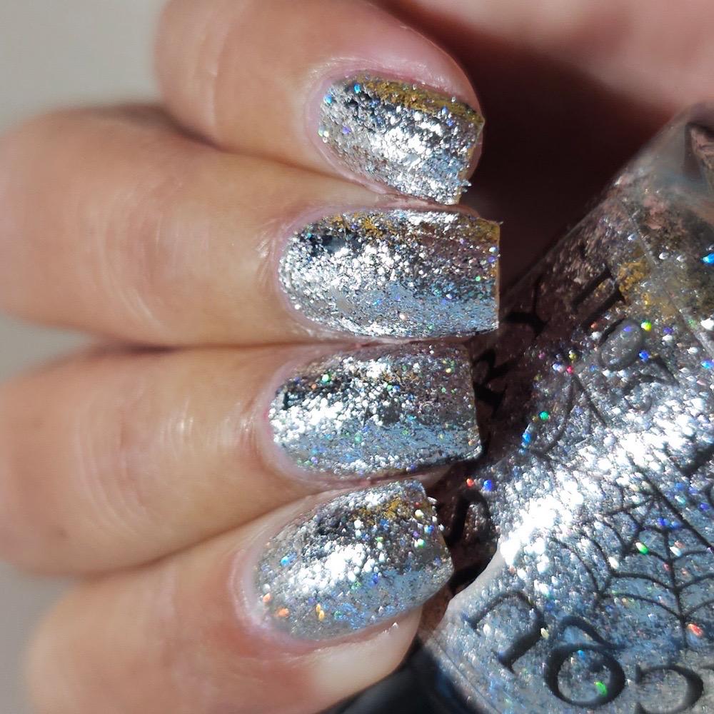 A close-up of a hand with nails painted in a shiny silver glitter nail polish, with the bottle of polish partially visible on the right.