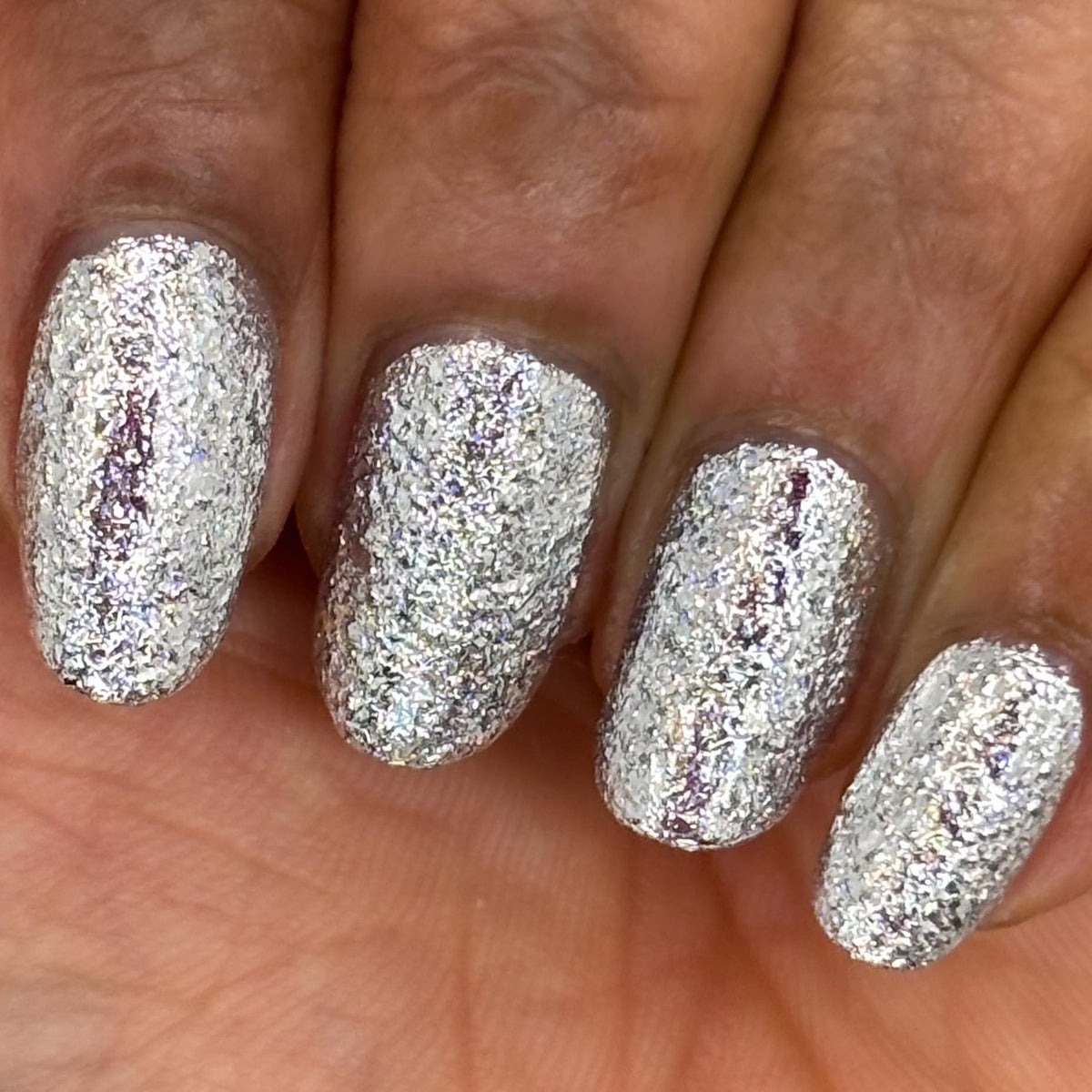 A close-up of a hand with nails painted in a shiny silver glitter nail polish,