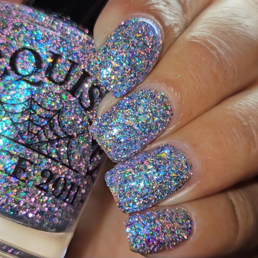 Close-up of a hand with nails painted in a dense holographic glitter nail polish, with the matching bottle partially visible in the background.