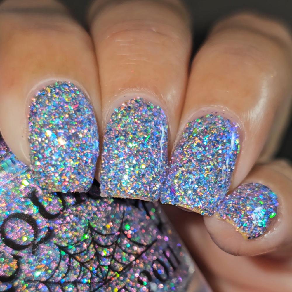Close-up of a hand with manicured nails painted in a dense, iridescent holographic glitter polish, with the matching glitter nail polish bottle visible at the bottom left.